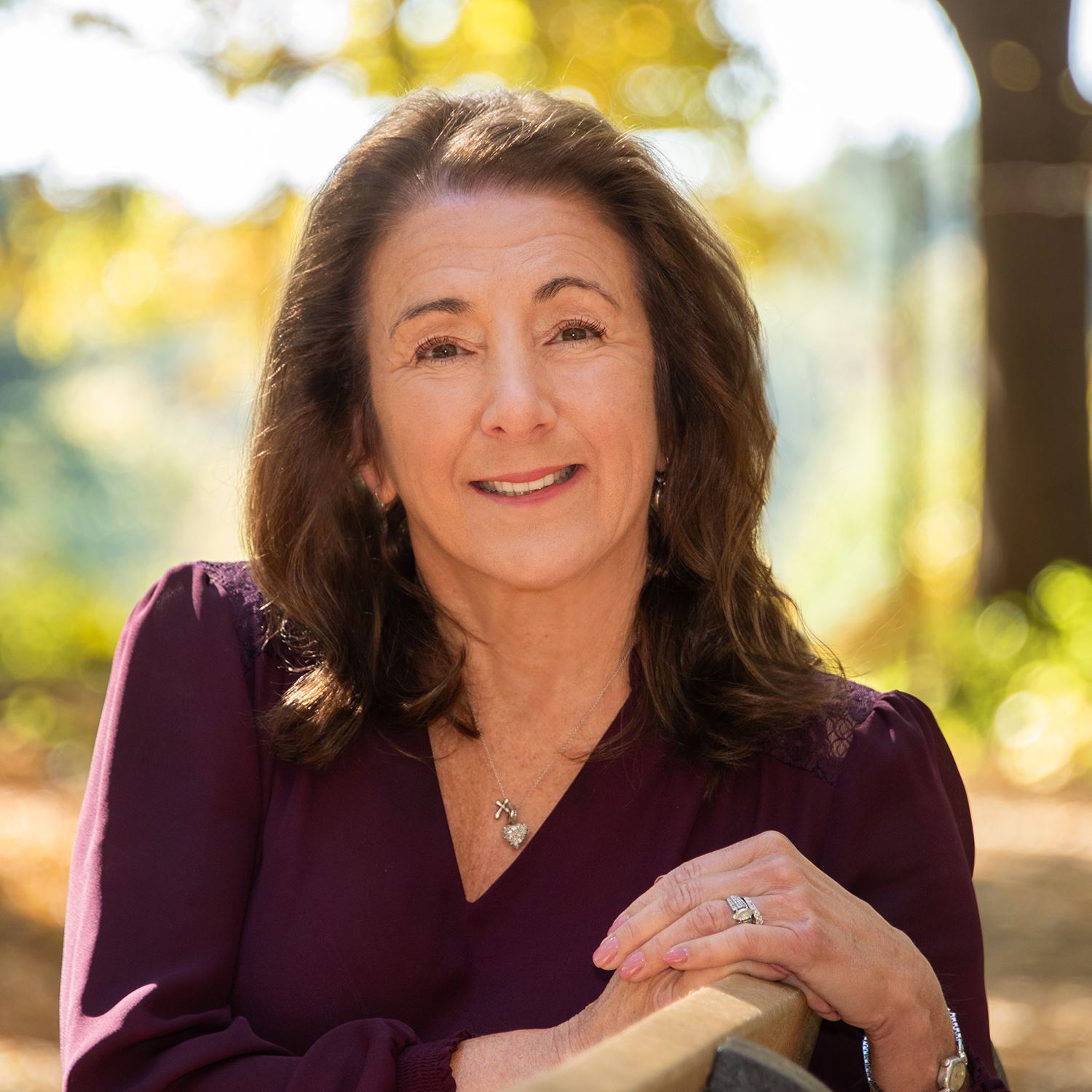 A photograph of a smiling brunette woman sitting outside