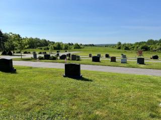 Cemetery gravestones lined up in rows, green rolling meadow with tree borders the background