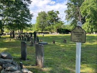 Pinkerton Graveyard sign, with rows of gravestones and green trees in the background